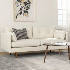 a living room with a white couch and coffee table in front of a painting on the wall