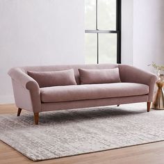 a pink couch sitting on top of a wooden floor next to a white rug and window