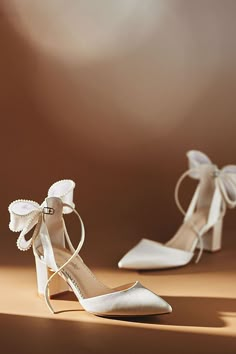 two pairs of white shoes with bows on the toes and heels are shown in front of a light brown background