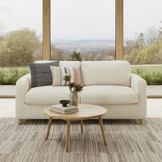 a living room scene with focus on the couch and coffee table in front of large windows