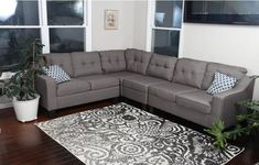 a living room with a gray sectional couch and potted plants on the floor in front of large windows