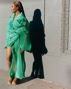 a woman in a green dress standing next to a white wall with her shadow on it