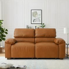 a living room with a brown leather couch and potted plant on the side table