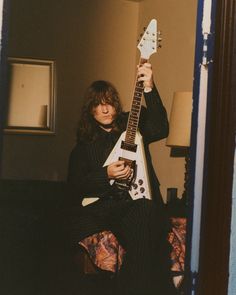 a man holding an electric guitar in his hand while sitting on a couch next to a lamp