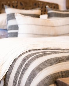 a bed with striped sheets and pillows on top of it, next to a wooden headboard