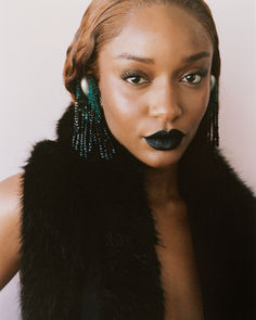 a woman with black lipstick and green beads on her face, wearing a fur vest