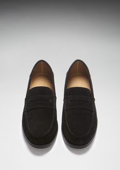 Here we offer you another Hugs & Co. take on a classic style. Our penny loafer upper made with carefully selected black Italian suede is teamed with a robust boat shoe sole in matching black rubber. This gives the shoes great wearability, fantastic comfort and the timeless style you're looking for in a penny loafer. We also offer loafers with tassels and driving shoes here at the Hugs & Co. online store. Our men's shoes are super cool and made to the tip top highest standards with leathers and suedes from England and Italy. If you're after preppy shoes or men's moccasins then you've come to the right place. UK Sizing Made in Portugal 100% Suede Upper featuring a 100% Leather Lining Rubber studded sole Classic Black Suede Oxfords, Classic Black Suede Leather Shoes, Classic Black Suede Dress Shoes, Black Suede Dress Shoes For Work, Black Suede Loafers With Stitched Sole, Black Moccasins With Suede Lining For Work, Black Suede-lined Moccasins For Work, Black Suede Lined Moccasins For Work, Black Suede Leather Shoes For Business Casual