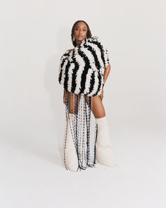 a woman standing in front of a white background wearing a black and white outfit with chains on it