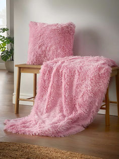 a pink fluffy blanket sitting on top of a wooden chair next to a table with a potted plant