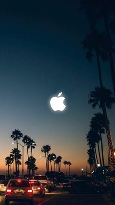 an apple logo is seen in the sky above palm trees at night, with cars parked on the street below