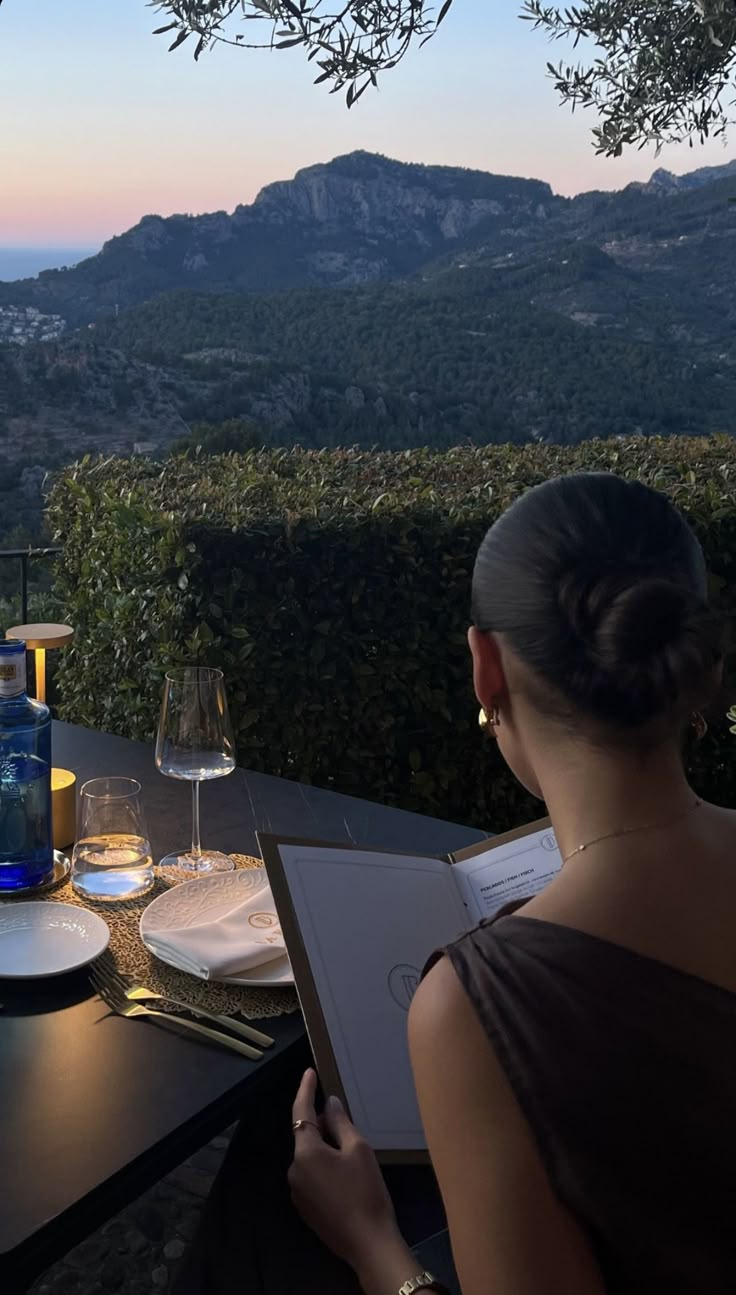 a woman sitting at a table with wine glasses and an open book in front of her