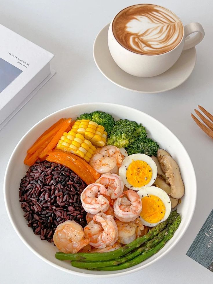 a white bowl filled with different types of food next to a cup of coffee