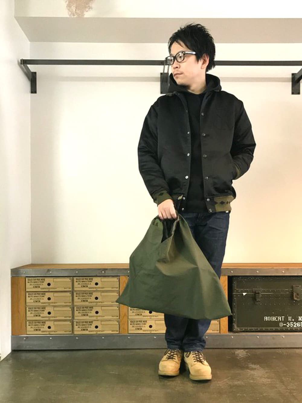 ブラック系のスタジャン、ブルー系のデニムパンツ、グリーン系のトートバッグを着用したメンズの冬コーディネートの1枚目の写真