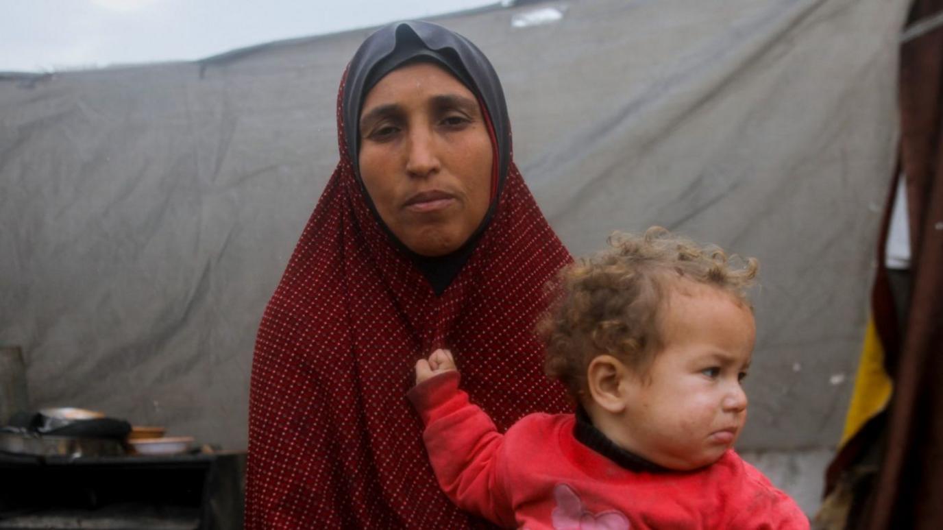 A Palestinian woman holds her child outside their makeshift shelter in Jabalia, northern Gaza