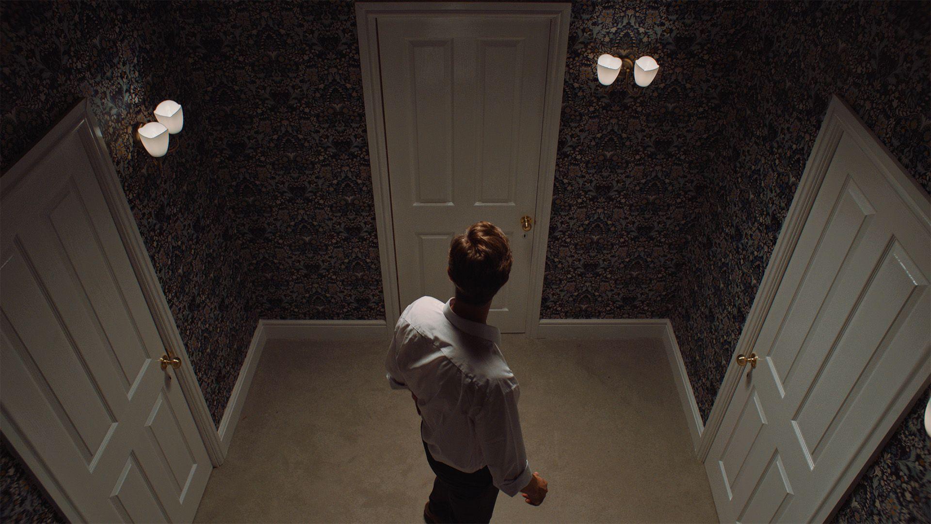 A man stood alone in a room facing a choice of several doorways.