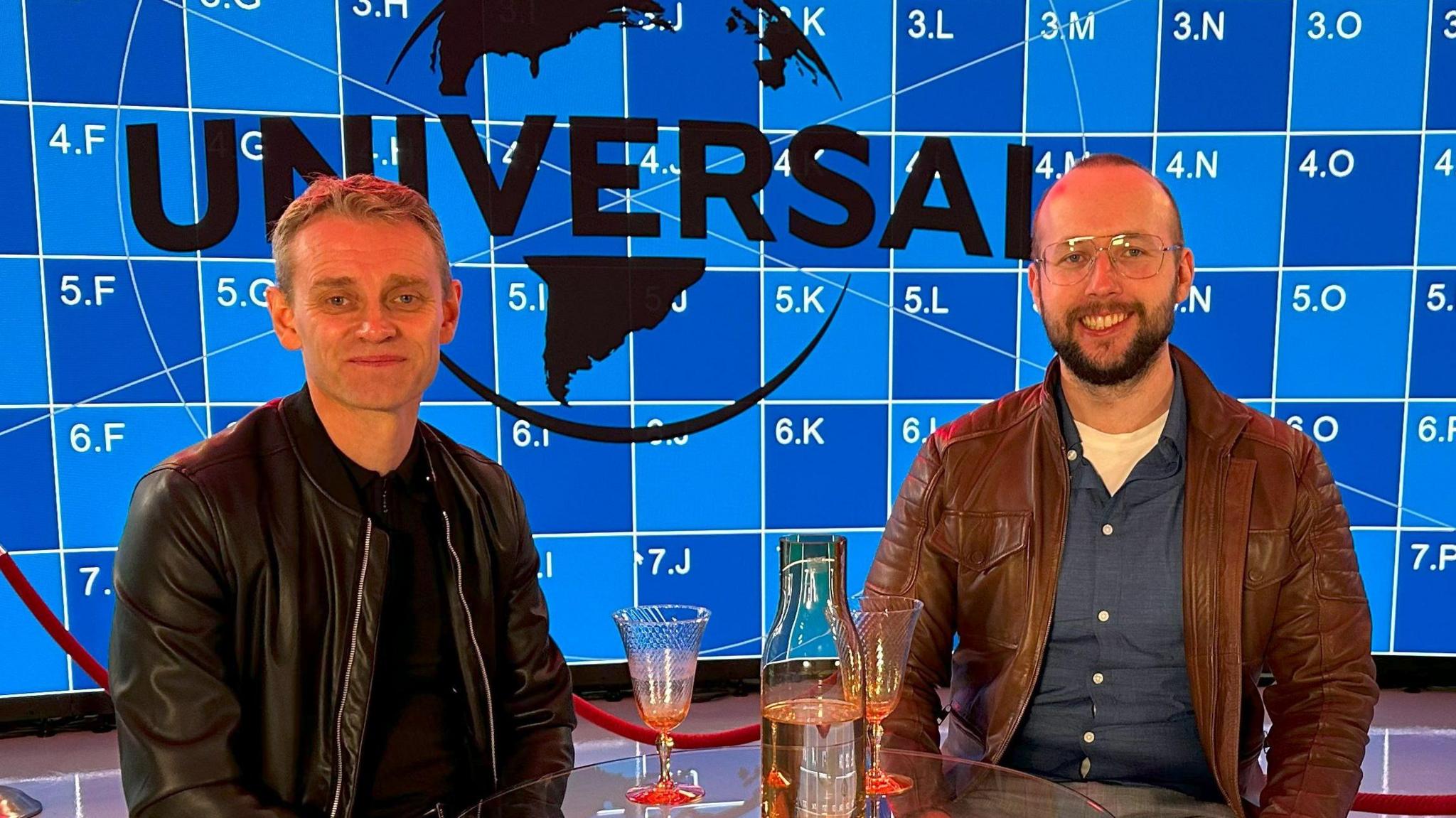 Two smartly dressed men stand side by side in an office/studio.