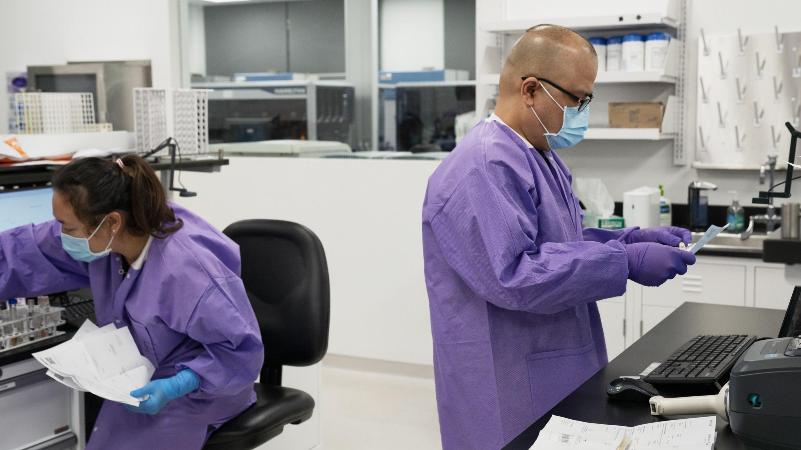 Lab workers in purple lab coats examine tests