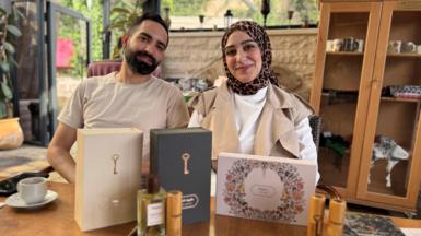 Qassem Abu Khalaf and his wife Malak Hijaz with a range of their perfumes on a wooden table.