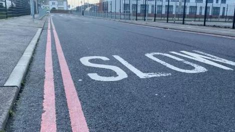 Double red lines on a quiet road that also has "SLOW" written on it in large white letters. There is also a school-style building surrounded by a fence in the background