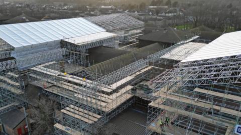 The H-shaped hospital building is surrounded by scaffolding as well as a huge canopy over the far left, long stretch of the hospital, which allows work to be done in all weathers beneath it. The picture is taken from above the hospital by a drone and gives a sense of the scale of the work being done.