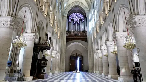 Notre Dame Cathedral, wide view that shows the tiled floor, ornate stonework and the organ below purple stained glass windows