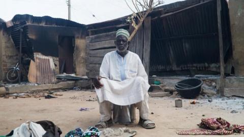 A man sits in front of burnt out remains in a Woro village in Nigeria