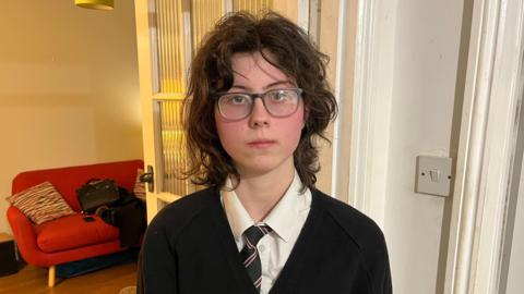 Portrait photograph of Martha, a 16-year-old girl, with a neutral expression and wearing her Reepham High School uniform. 