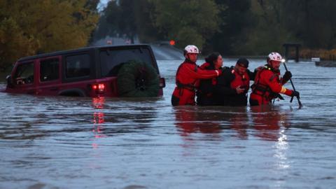 Rescuers lead a woman to safety from a car in a flooded road