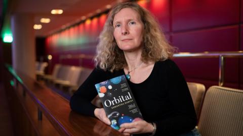 Samantha Harvey holding her novel, Orbital