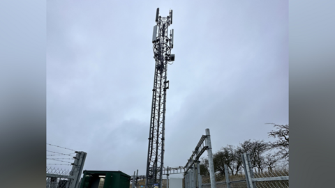 The mast tower with fencing around it on a cloudy day.