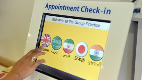 A woman's hand presses a touch screen to access a GP appointment