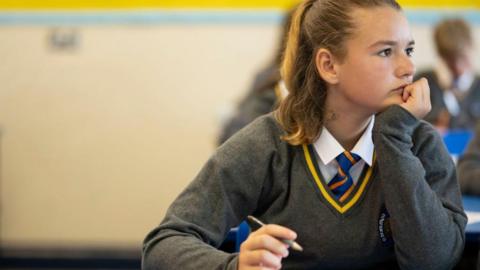 A pupil listens during a history lesson at Whitchurch High School on September 14, 2021 in Cardiff, Wales. The teenager is wearing a grey jumper, with a white shirt and blue and orange striped tie. 