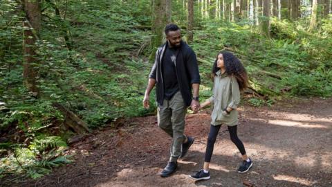 A father and daughter walking hand in hand through the woods