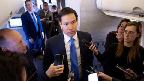 Mark Rubio in a suit and blue tie surrounded by reporters