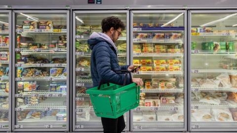 A man standing next to a supermarket freezer section