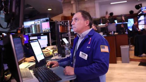 A trade on the New York Stock Exchange anxiously looks at screen with share prices