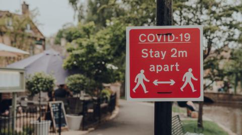 Red Covid-19 Stay 2 Metres Apart sign on a footpath