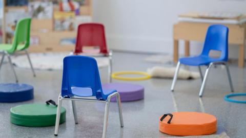 An empty classroom ready for primary school pupils. The class is full of colourful seats, chairs, books, toys and educational posters.