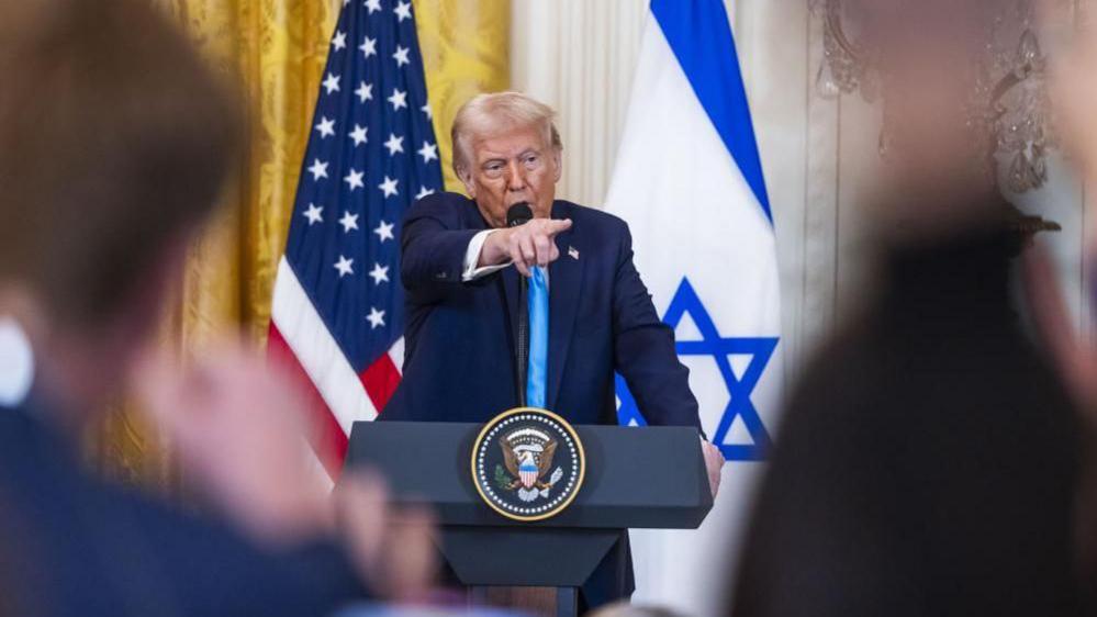 Donald Trump at a podium in front of the US and Israel flags during a press conference 