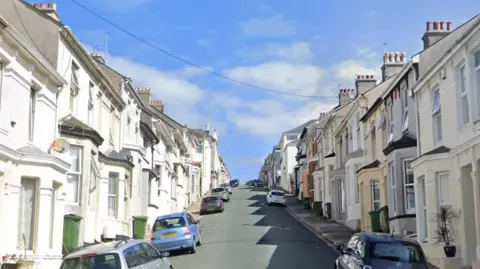 Google image of Townshed Avenue in Plymouth. Residential properties line either side of the road which is on a hill. Cars are parked along the road. 