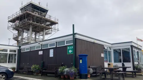 A one storey building with an airport watch tower on a cloudy day.