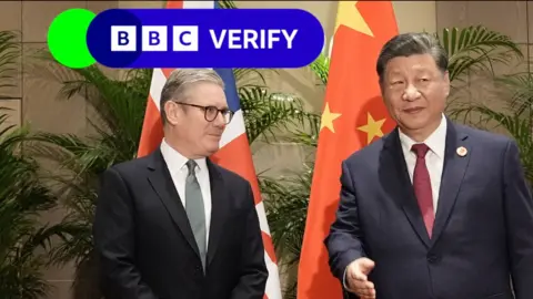 Prime Minister Sir Keir Starmer stands in front of a UK flag and next to President Xi Jinping of China, who is in front of a Chinese flag. Starmer is looking at Xi, who is looking away