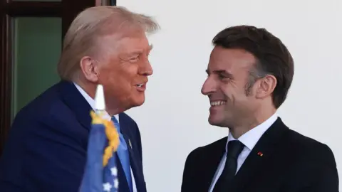 Donald Trump and Emmanuel Macron grin at one another.