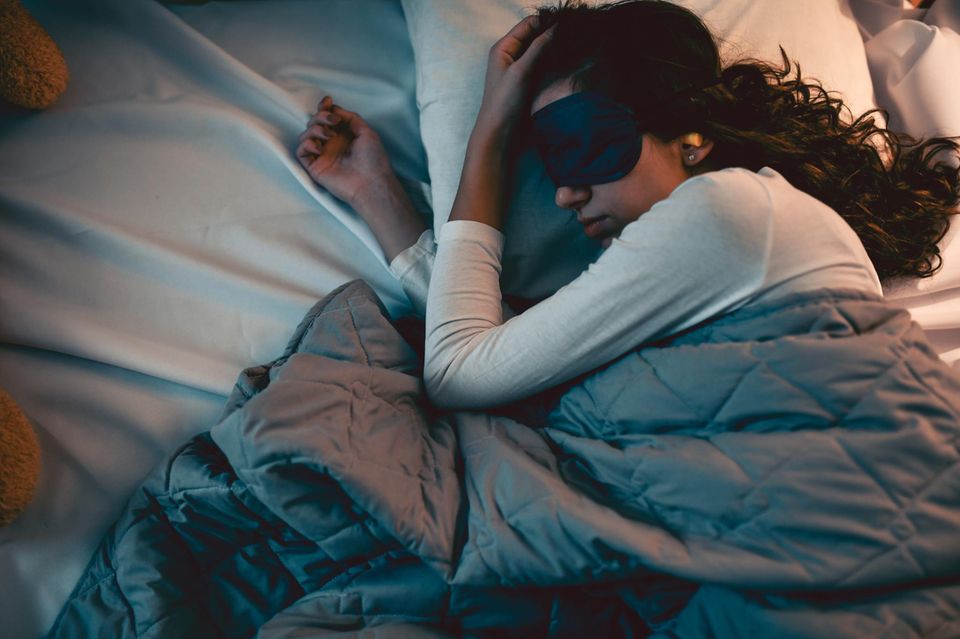 Frau im Bett mit Schlafmaske und Ohrenstöpseln