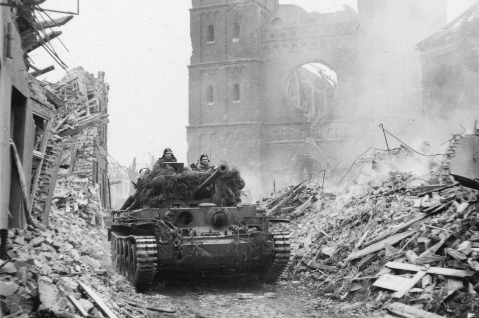 Ein Panzer fährt in einer Stadt zwischen Trümmern hindurch