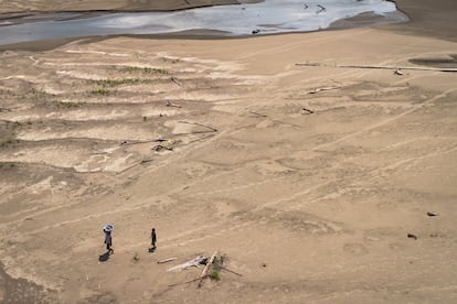 Artea Pérez y su hijo caminan con sus productos bajo el sol por la playa seca por la sequía de regreso a su comunidad en Perú, el 16 de octubre de 2024.