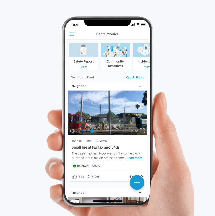 Hand holding a smartphone displaying the Neighbors by Ring app, showing local safety updates, video posts, and community alerts for Santa Monica.