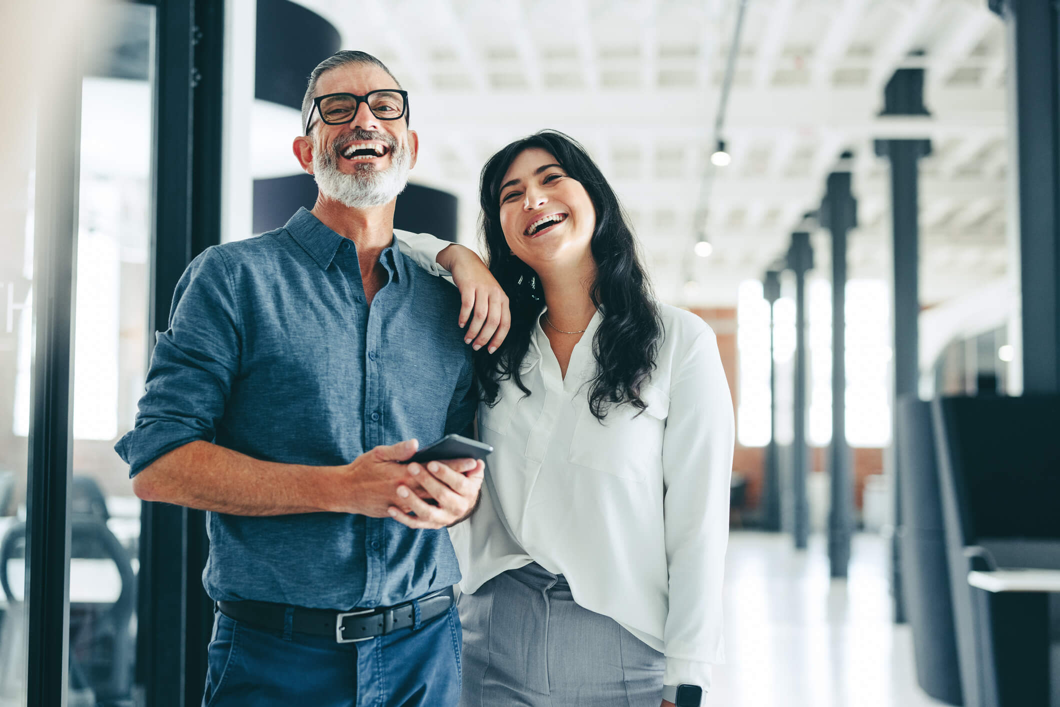 A man and woman are laughing while standing in an office.