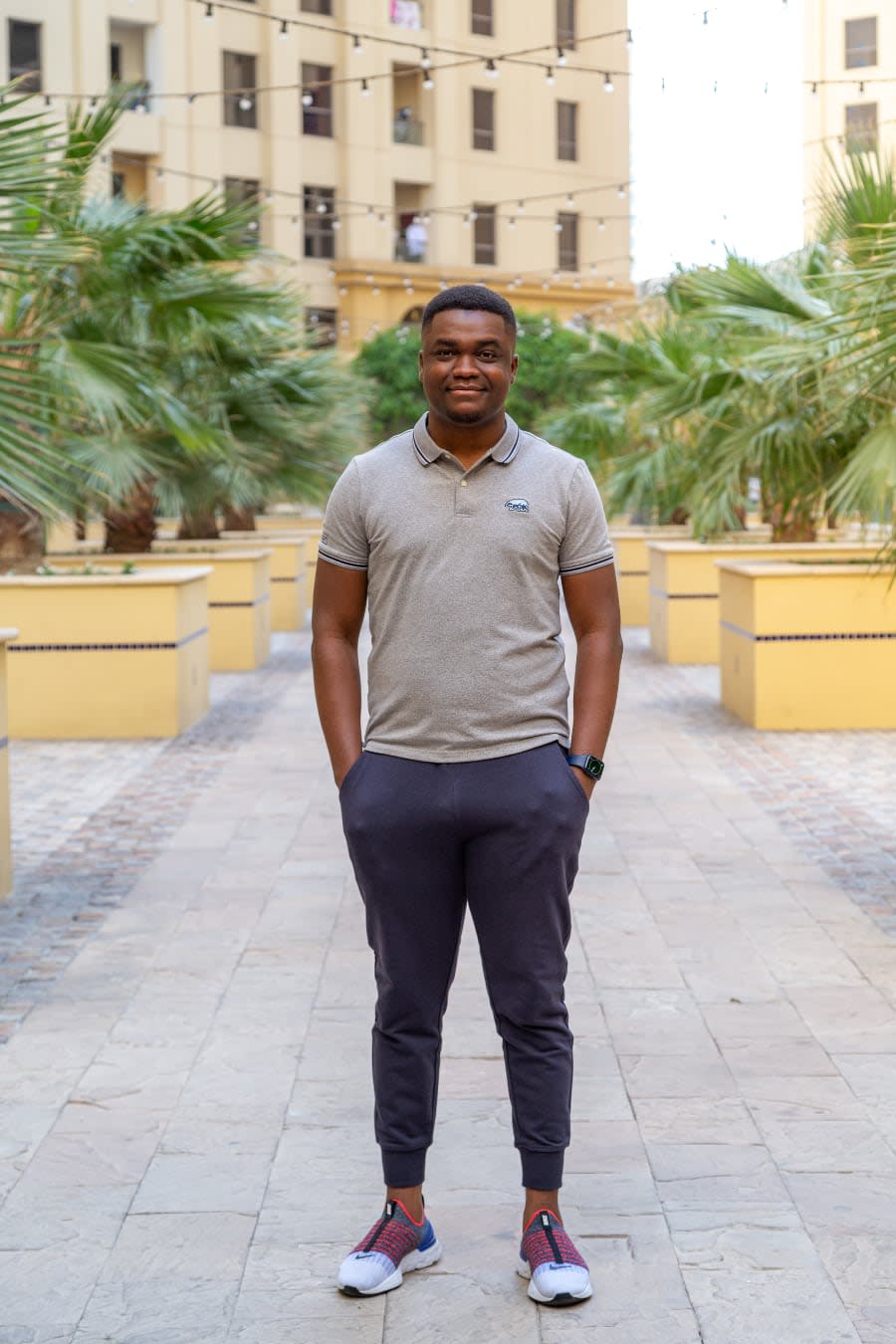 Portrait of Segun Adebayo standing outdoors between plamtrees.