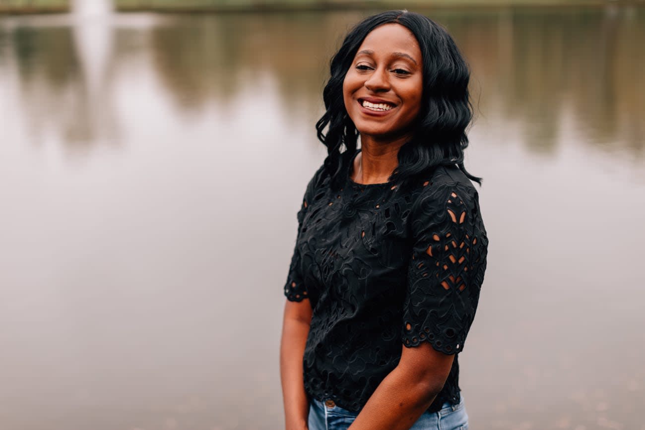 Photo of Monica Powell outdoors, next to a lake, smiling.